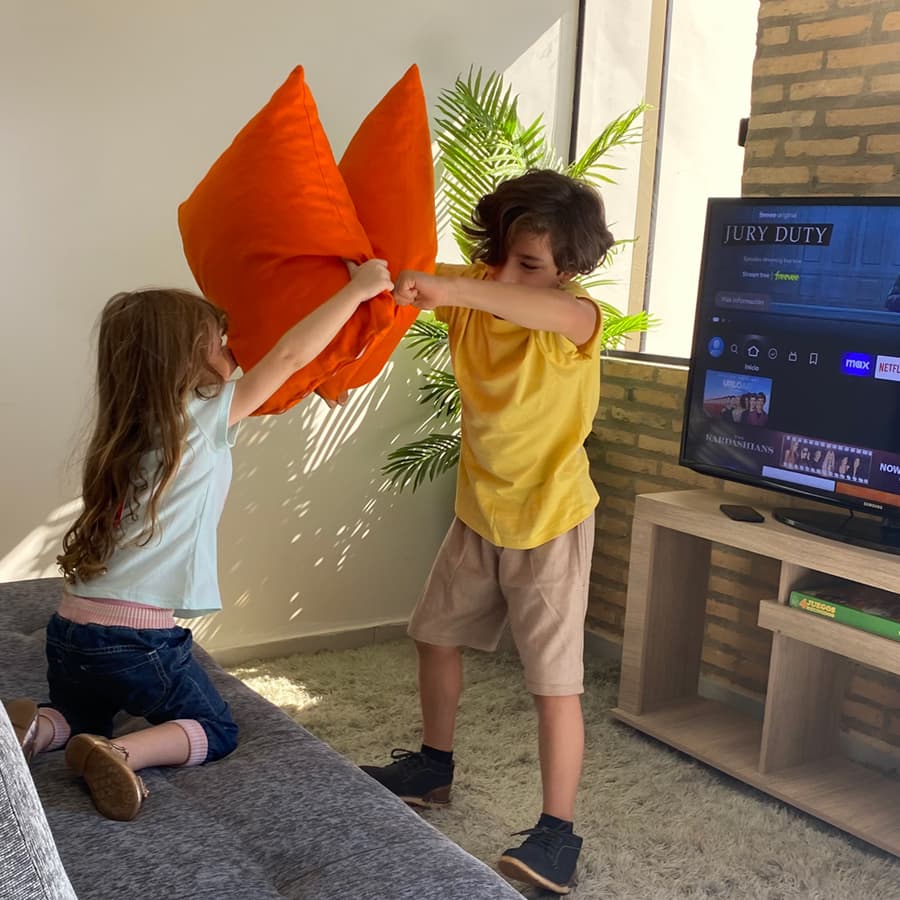 Hija y hija jugando a la lucha de almohadas en el living de casa más