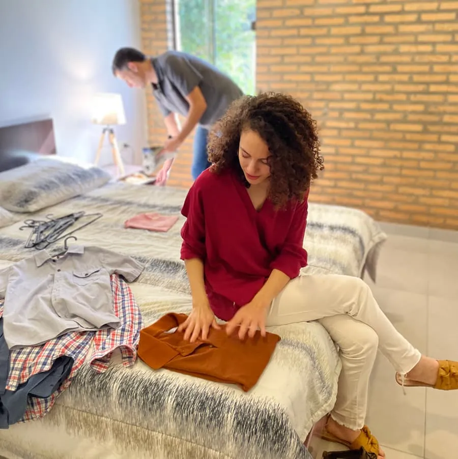 mamá doblando ropas en la cama del dormitorio de casa más, papá guardando algo en la mesita de luz